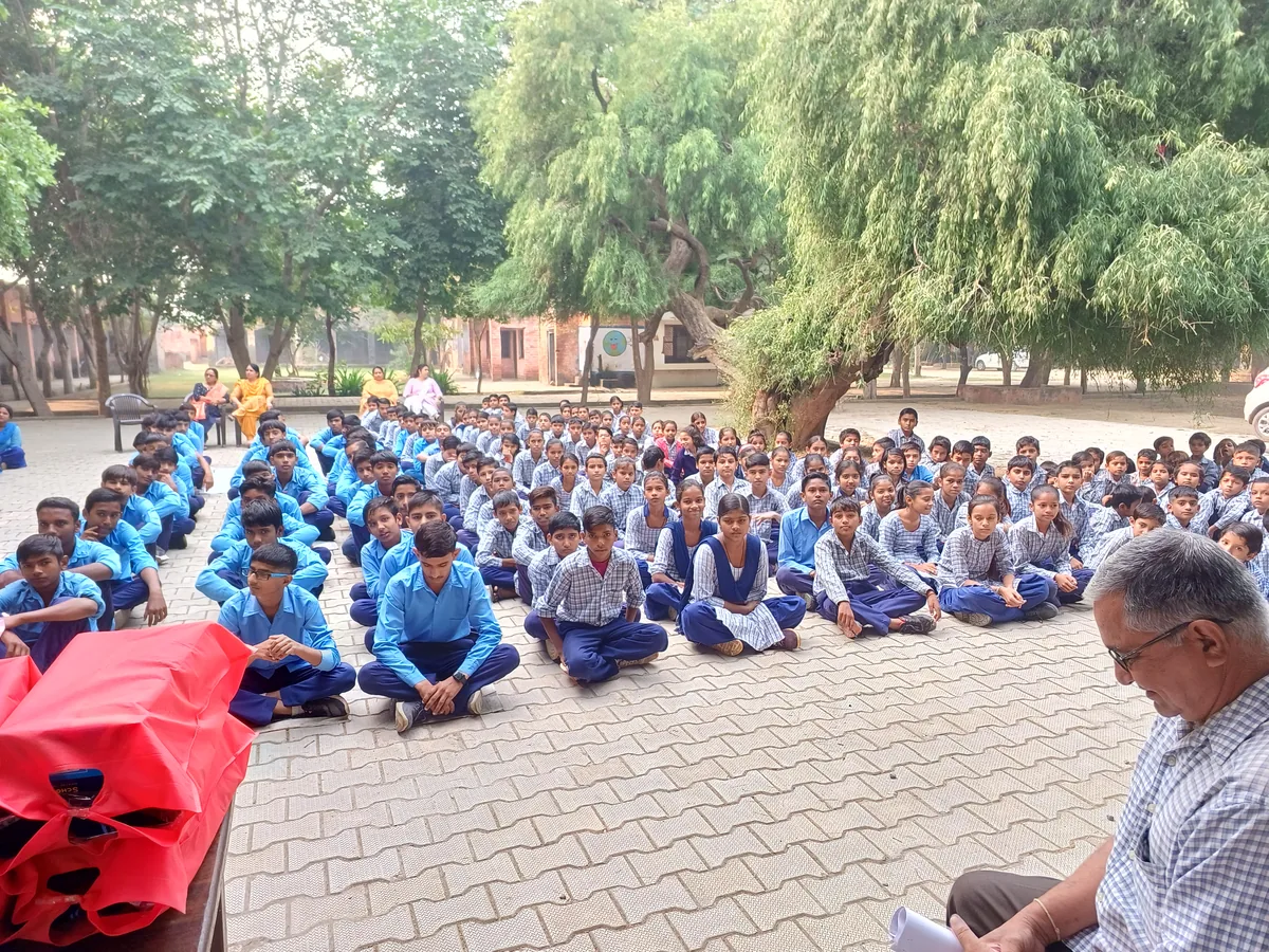 Students seated on the school courtyard beside stacks of red winter jackets