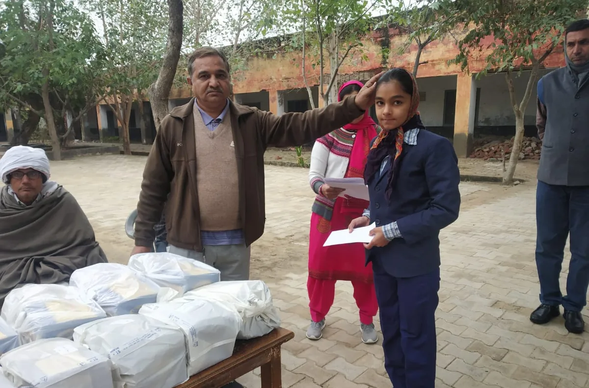 A volunteer blessing a schoolgirl beside a table of winter clothes