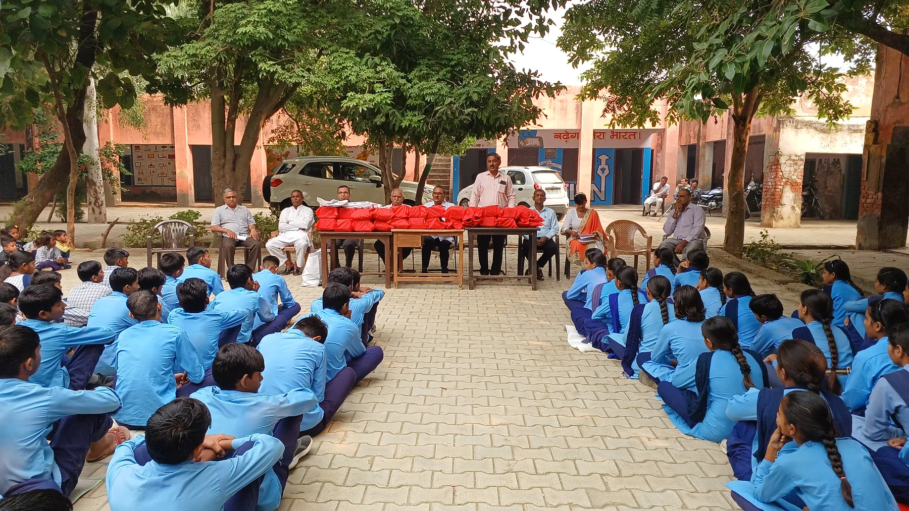 Volunteers behind tables of red winter jackets, with students seated in rows at Gaddi Kheri school