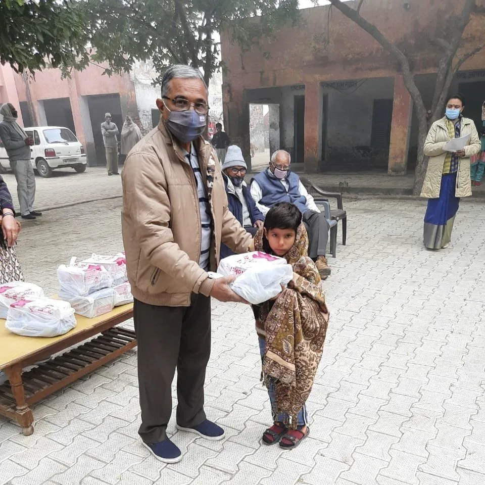 A volunteer handing winter clothes to a child wrapped in a shawl