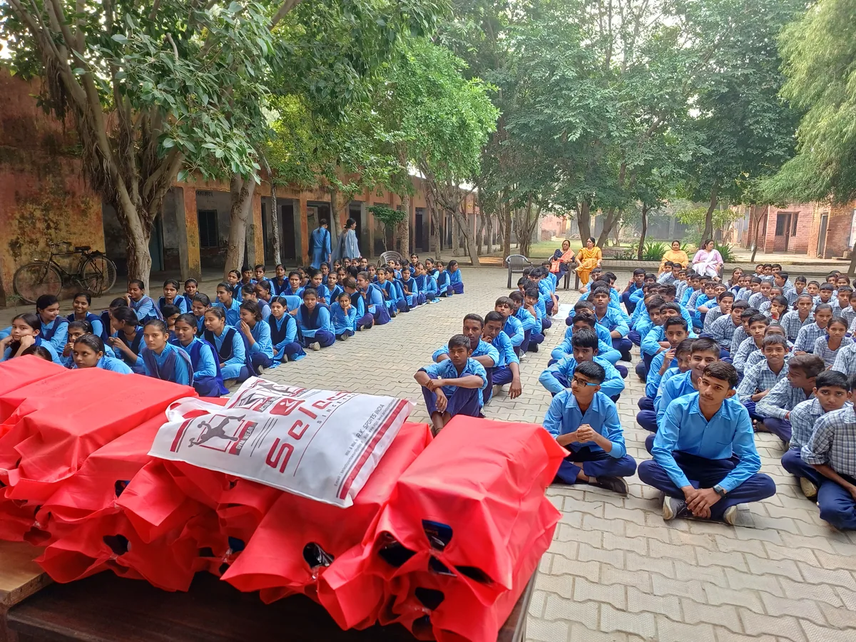 Stacks of red winter jackets in front of students seated in rows at Gaddi Kheri school