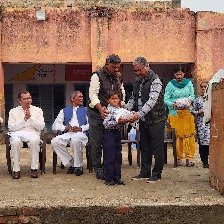 Volunteers handing winter clothes to a child at Gaddi Kheri school