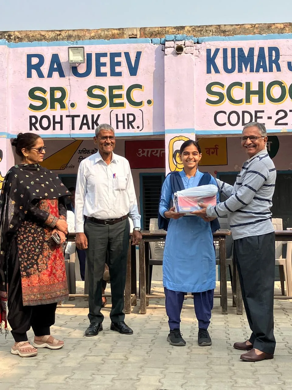 Volunteers presenting a bundle of winter clothes to a schoolgirl, 2025