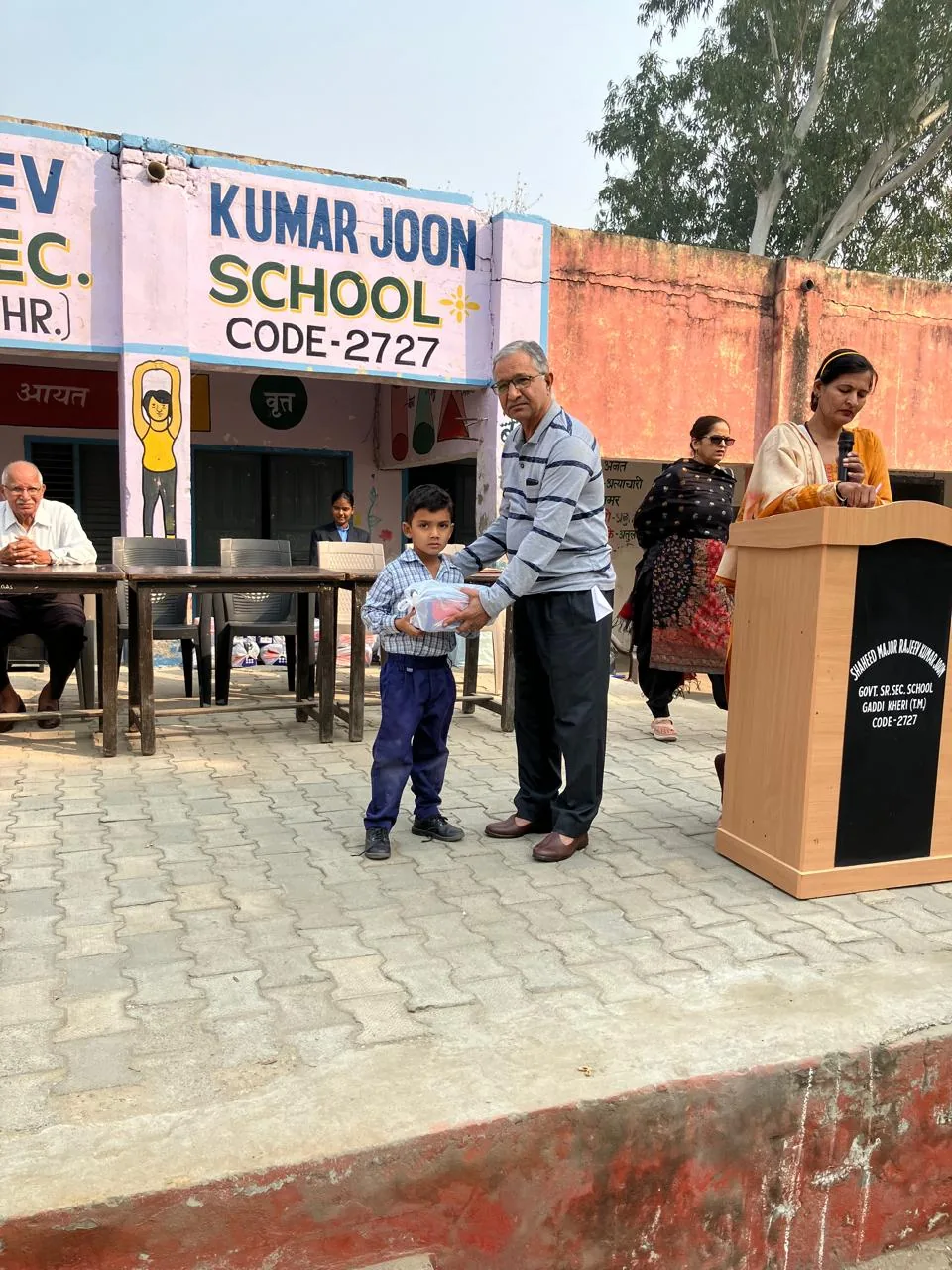 A volunteer handing a bundle of winter clothes to a young boy at school, 2025
